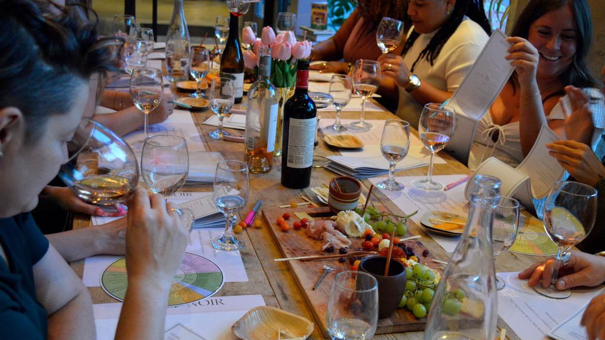 A long dining table filled with the Savvy Llama wine tasting experience kit being shared with friends. The tasting structure, tablescape, tasting notes, aroma wheel. Wine bottles, glasses and wine accessories, charcuterie on the table.